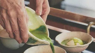 Person pouring green tea into ceramic bowls.