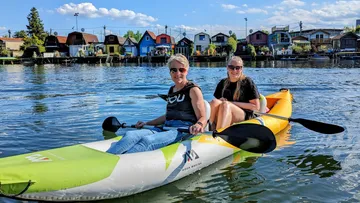 People kayaking on a calm river, colorful houses behind.