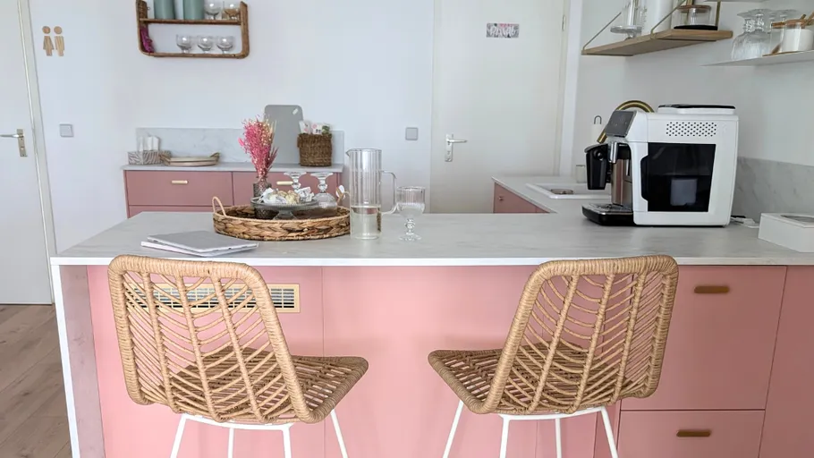Küche mit rosa Schränken und Korbstühlen.