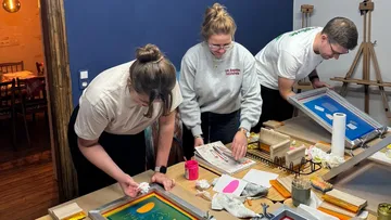 Three people screen printing at a workshop.