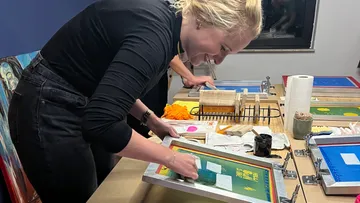 Person screen-printing artwork on wooden table.