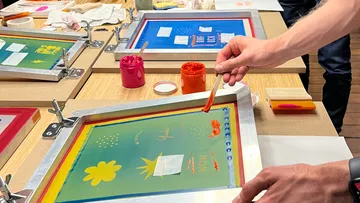 Person screen printing on wooden table.