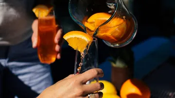 Person gießt Orangengetränk in Glas draußen ein.