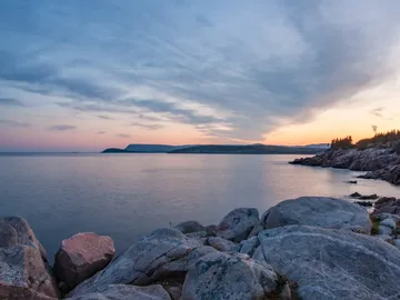 Rocks lie on the calm, wide sea at sunset.