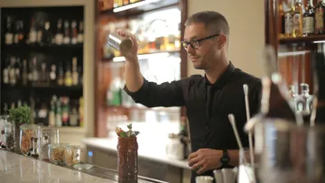 Barkeeper schüttelt Cocktail-Shaker an Bar.