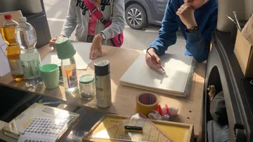 People drawing at a table in a van.