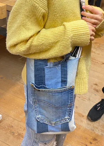 Person im gelben Pullover, trägt Jeans-Tasche.