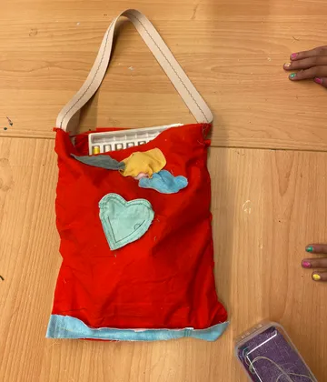 Handgefertigte rote Tasche mit bunten Aufnähern, Holztisch.