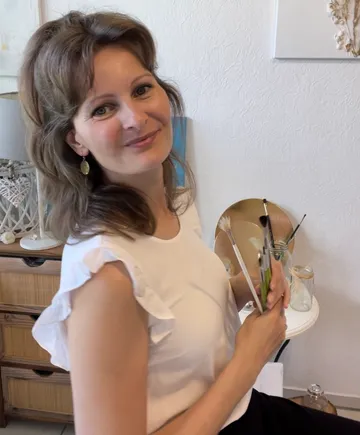 Woman holding paintbrushes, smiling indoors.
