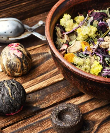 Dried herbs in a bowl on wooden table.