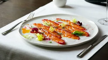 Salmon carpaccio garnished with herbs on plate.