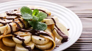 Crepes with bananas, chocolate, mint garnish on plate.