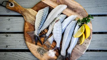 Six fish with lemons on round wooden board.