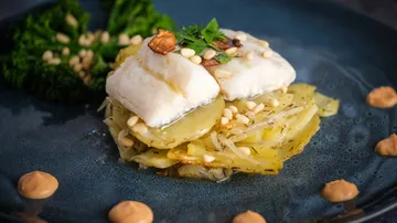 Fish on potato stack with greens and sauce.
