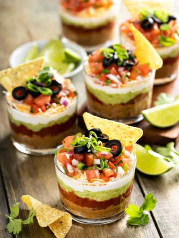 Layered dip in glasses with tortilla chips.
