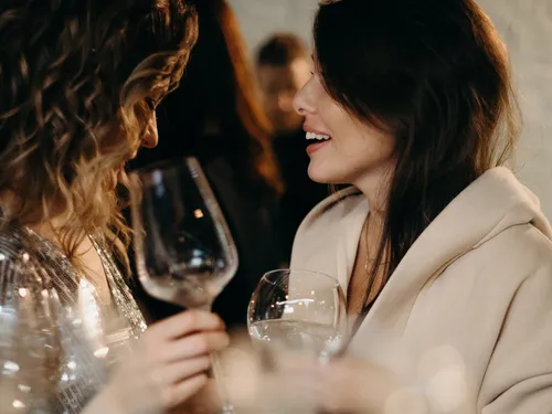 Two women are talking and holding wine glasses.
