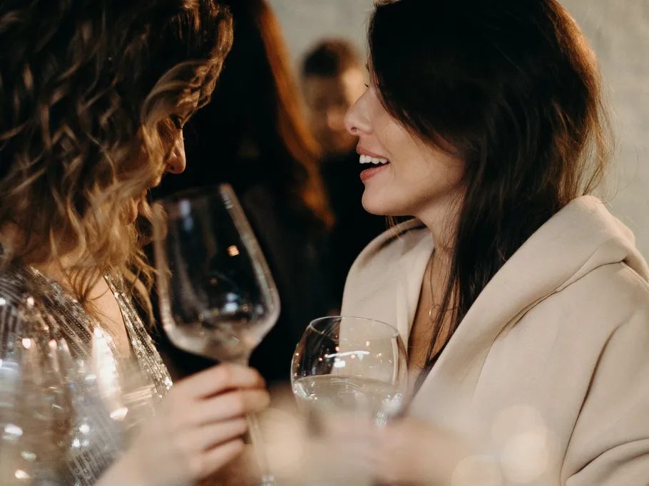 Two women are talking and holding wine glasses.