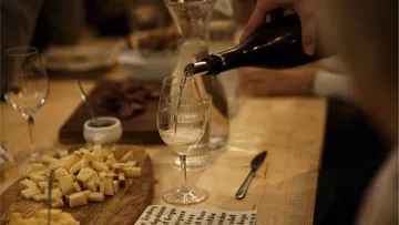 Person pours wine into glass on table.