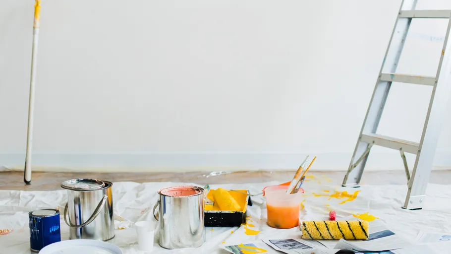 Malerausrüstung mit Farbrollen, Pinseln und Leitern auf Plane.