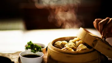 Steamed dumplings in bamboo basket with sauce.