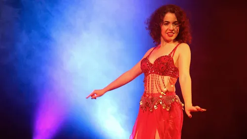 Woman belly dancing on stage with colorful lights.