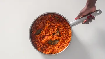 Hand holding pan with jollof rice inside.