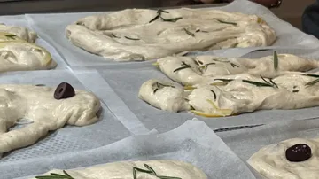 Ungebackener Focaccia-Teig mit Rosmarin auf Blechen.