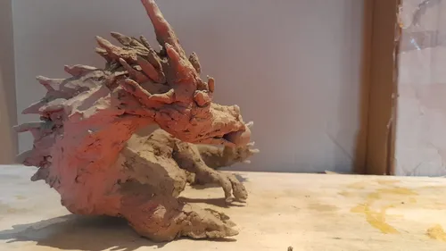 Drachenskulptur aus Ton auf Holzoberfläche.