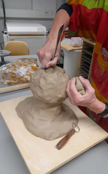 Person sculpting clay bust in a workshop.