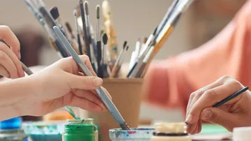 Hands painting with brushes in a studio.