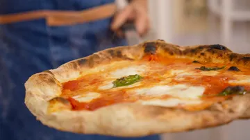 Pizza wird gehalten, unscharfer Hintergrund.