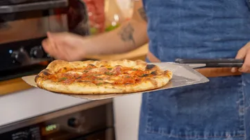 Person hält frisch gebackene Pizza auf Schieber.