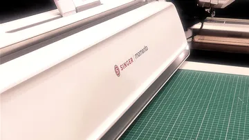 Weiße Nähmaschine auf einer grünen Matte.