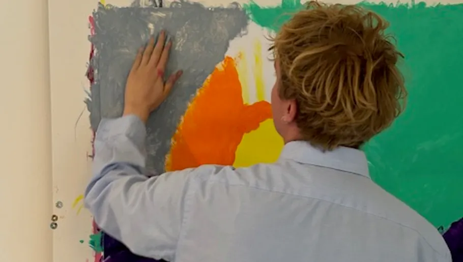 Person malt abstrakte Kunst an einer Wand.