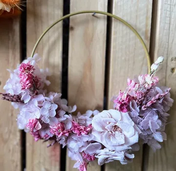 Blumenkranz mit rosa Blumen an Holzwand.