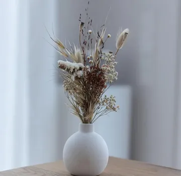 Trockenblumenarrangement in weißer Vase auf Tisch.