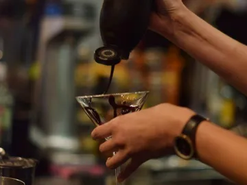 Eine Hand gießt Schokoladensauce in ein Cocktailglas.