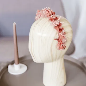 Hölzerner Puppenkopf trägt Blumenkrone.