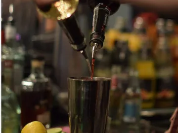 Zwei Flaschen gießen Liköre in einen Shaker auf der Bar.