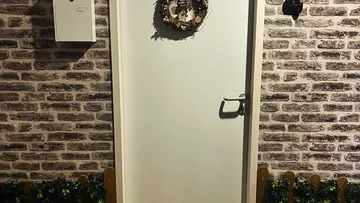 Weiße Tür mit Kranz, Ziegelwand Hintergrund.
