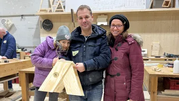Family in workshop holding wooden project.