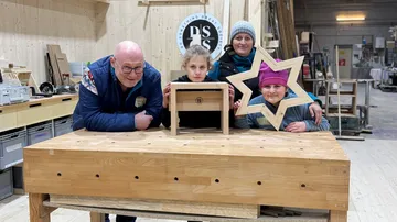Four people posing with wooden creations in workshop.