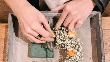 Hands arranging flowers in a wooden box.