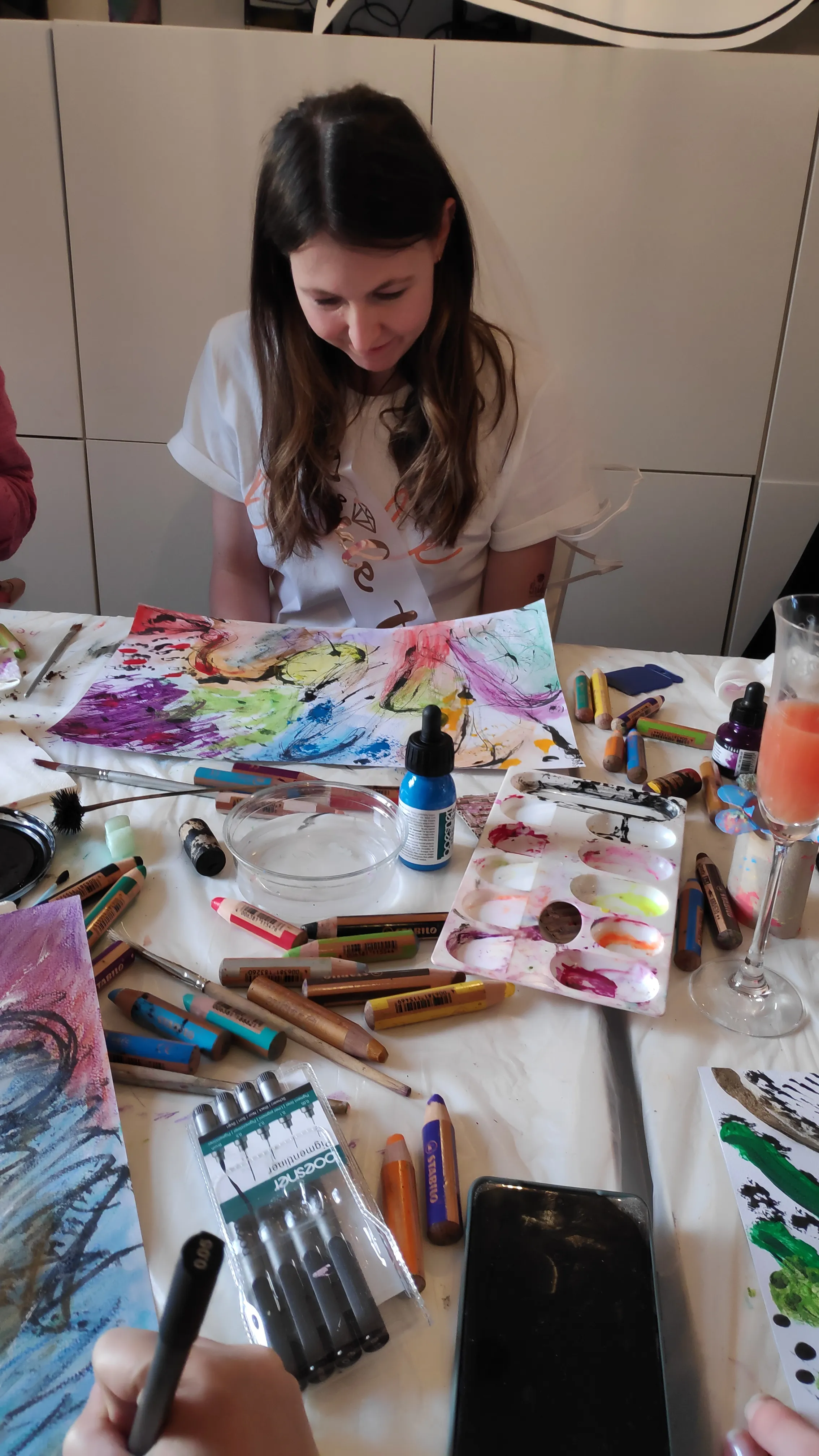Woman painting at table with art supplies.