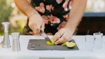 Person schneidet Limette auf Schneidebrett draußen.