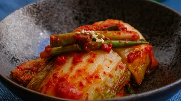 Kimchi in einer dunklen Schale auf Tisch.