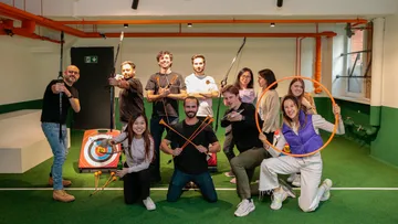 Group posing with archery equipment indoors.