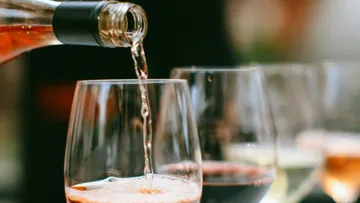 Wein wird in ein Glas gegossen, unscharfer Hintergrund.