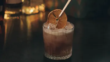 Cocktail with dried orange garnish on bar.