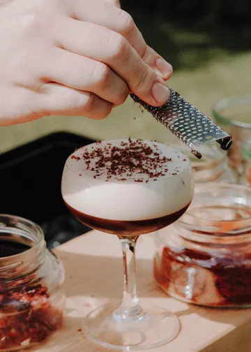 Hand reibt Schokolade über Cocktailglas.